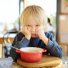 Unhappy boy doesn't want to eat the food in the bowl in front of him
