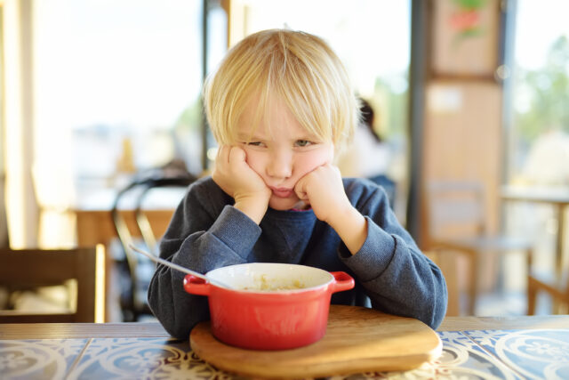 Unhappy boy doesn't want to eat the food in the bowl in front of him