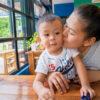 Asian mother kissing young child sitting at a table