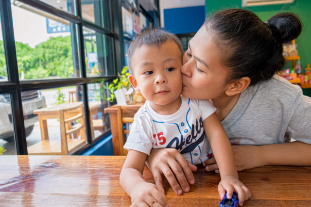 Asian mother kissing young child sitting at a table