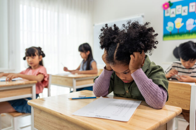 Frustrated Black girl in kindergarten taking test in school sitting at desk